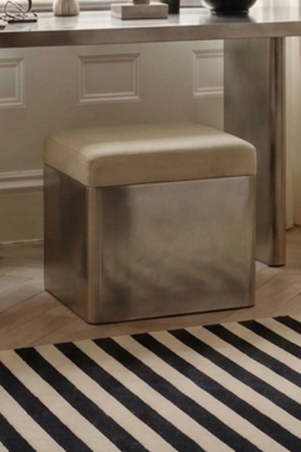 The Kasanai stainless steel stool tucked beneath a stainless steel dressing table, in a calm bedroom with a striped rug.